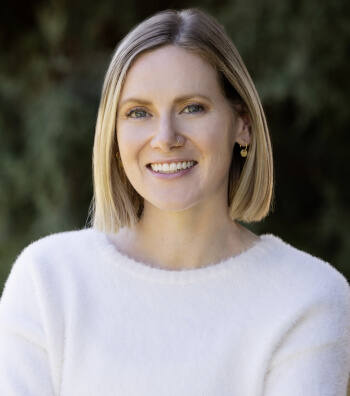 Portrait of Therapist Rebecca Newell, standing outside, wearing a white sweater, smiling